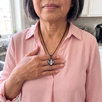 Thumbnail for Woman in a pink blouse warming the black clover pendant with her thumb to reveal the photo | SKU: TPH-CLVN-BLACK