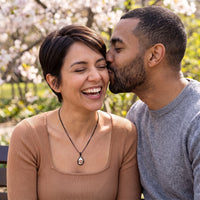 Thumbnail for Couple laughing under spring blossoms, she wears the black secret drop photo necklace | SKU: TPH-DRPN-BLACK