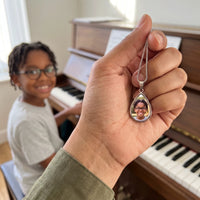Thumbnail for The silver teardrop photo pendant held up, real small size, a boy playing the piano behind | SKU: TPH-DRPN-SILVER