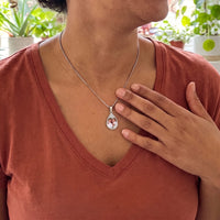 Thumbnail for Woman in a rust top with her hand on her heart, wearing the silver secret drop photo necklace | SKU: TPH-DRPN-SILVER