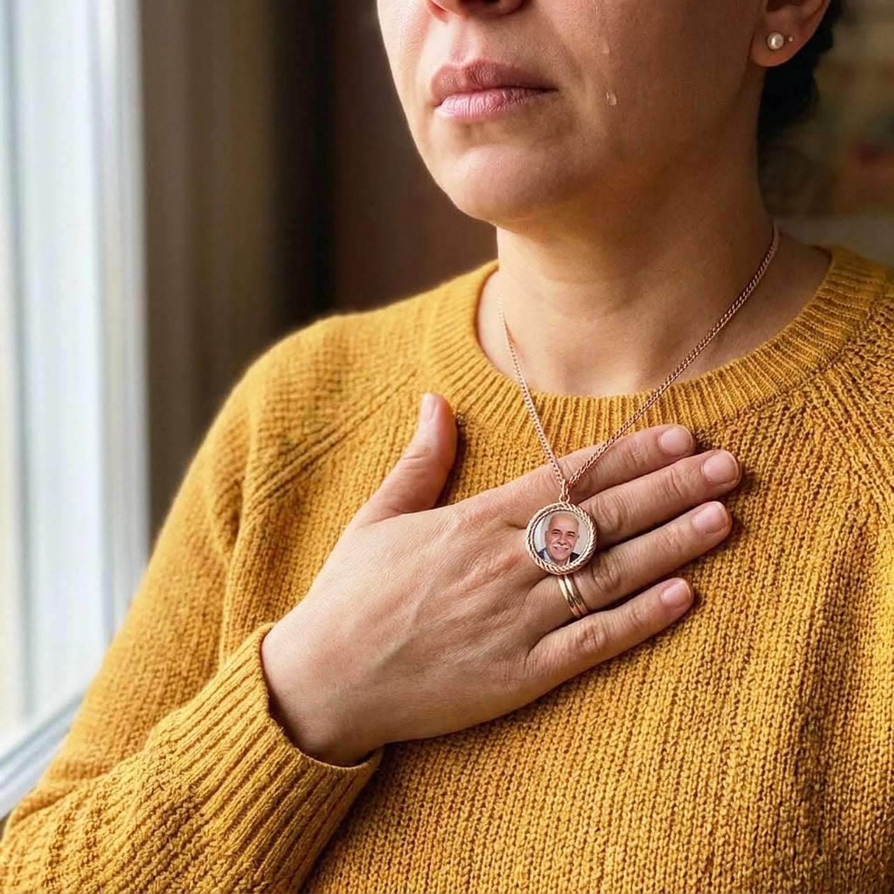 Woman moved to tears, her hand on the rose gold round photo necklace holding a late loved one's photo | SKU: TPH-RNDN-ROSEGOLD
